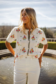 Pull fleuri à manches courtes porté par une femme, vue de face, fontaine, haies taillées