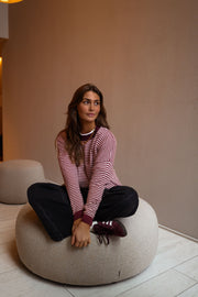 Pull rayé effet cachemire porté par une femme, assise, pouf beige, jambes croisées
