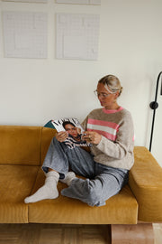 Pull rayé doux col rond porté par une femme, assise, sur un canapé jaune, magazine