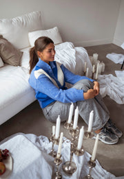 Pull à col montant boutonné bleu porté par une femme, assise, canapé, bougies