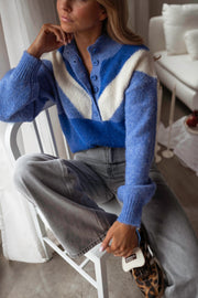 Pull à col montant boutonné bleu porté par une femme, vue rapprochée, chaise, pantalon gris