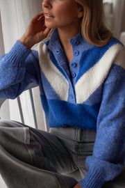 Pull à col montant boutonné bleu porté par une femme, vue rapprochée, main près du visage, chevrons