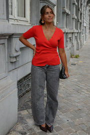Pull cache-cœur manches courtes porté par une femme, silhouette entière, jean gris, pochette à la main, mains sur les hanches