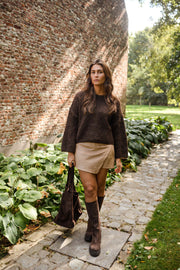 Pull à coutures apparentes marron porté par une femme, vue de face, allée pavée, bottes marron