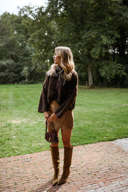 Pull à coutures apparentes marron porté par une femme, silhouette entière, pelouse, bottes marron