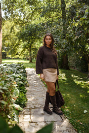 Pull à coutures apparentes marron porté par une femme, silhouette entière, chemin de jardin, mini-jupe