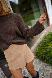 Pull à coutures apparentes marron porté par une femme, vue rapprochée, coutures apparentes, jupe beige
