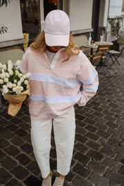 Pull ample à col polo porté par une femme, silhouette entière, casquette rose, bouquet de fleurs blanches