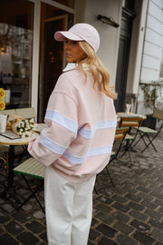 Pull ample à col polo porté par une femme, vue de trois-quarts, casquette rose, pantalon blanc, terrasse