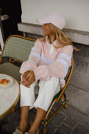 Pull ample à col polo porté par une femme, assise, casquette rose, sur une chaise de café