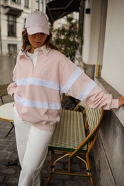 Pull ample à col polo porté par une femme, assise, casquette rose, bras tendu