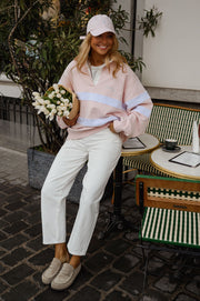 Pull ample à col polo porté par une femme, assise, casquette rose, fleurs blanches, pantalon blanc