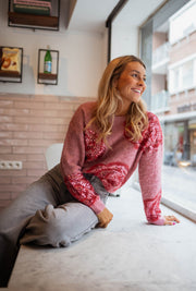 Pull doux à paillettes framboise porté par une femme, assise, mur rose, jambes croisées