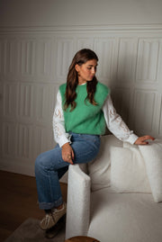 Pull sans manches doux vert porté par une femme, assise, canapé, jean bleu