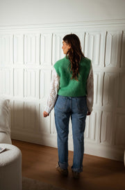 Pull sans manches doux vert porté par une femme, vue de dos, jean, boiseries