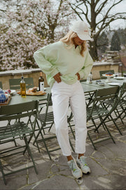 Pull à col boutonné porté par une femme, silhouette entière, casquette, terrasse