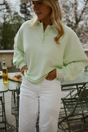 Pull à col boutonné porté par une femme, vue de trois-quarts, pantalon blanc, terrasse