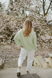 Pull à col boutonné porté par une femme, vue de dos, magnolias, pantalon blanc