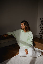 Pull à col boutonné porté par une femme, assise, sur le sol, intérieur sombre