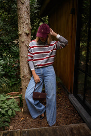 Pull rayé à col polo porté par une femme, vue de trois-quarts, sac bordeaux, casquette