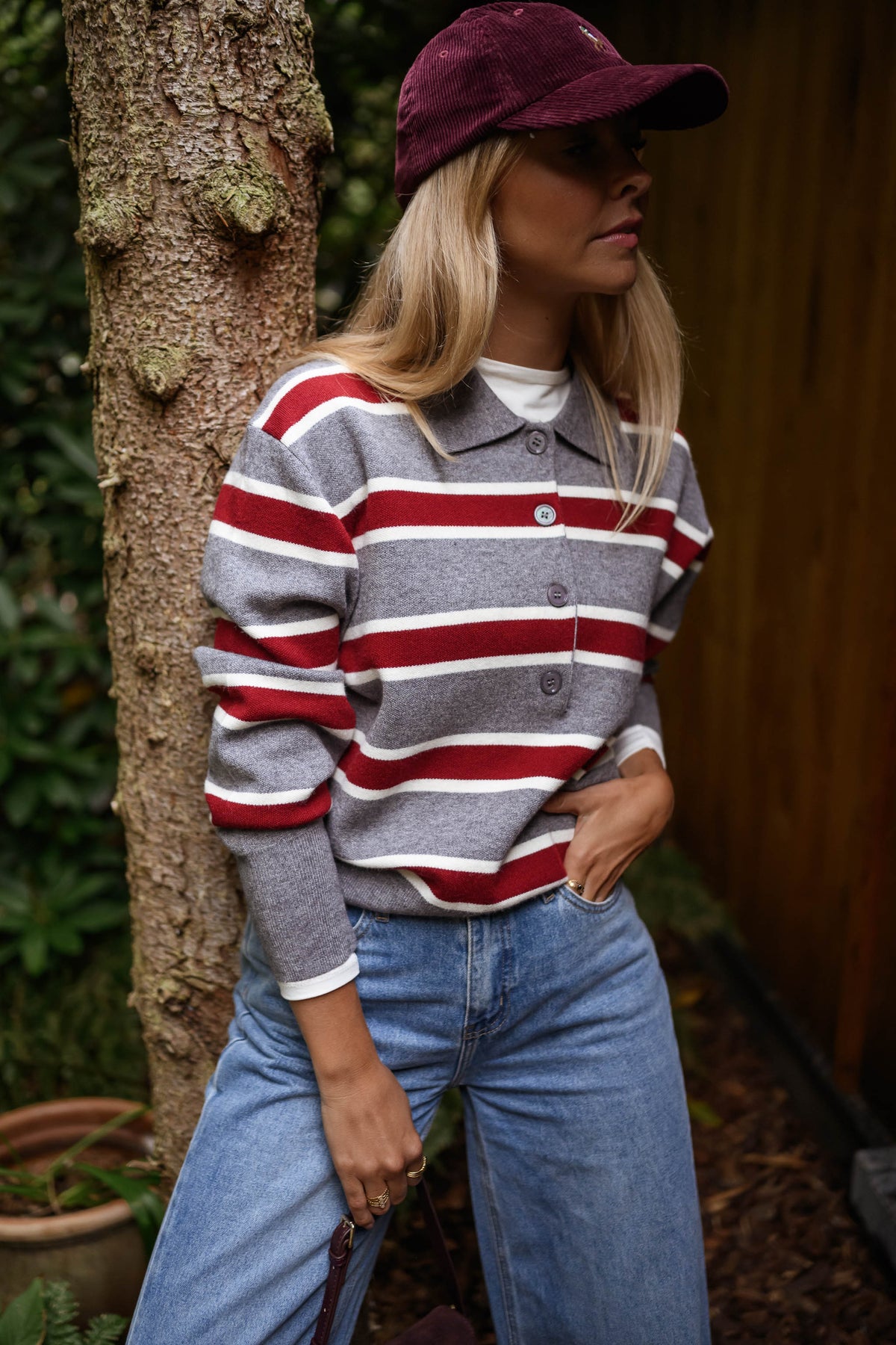 Pull rayé à col polo porté par une femme, vue de face, casquette bordeaux, tronc d'arbre