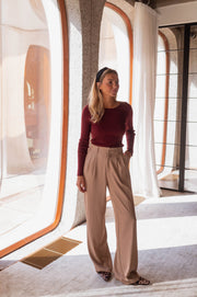 Pull moulant à boutons d’épaule bordeaux porté par une femme, silhouette entière, baie vitrée, pantalon beige, autre cadrage