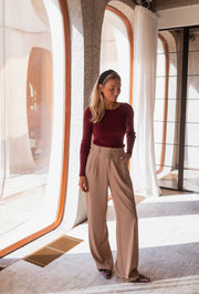 Pull moulant à boutons d’épaule bordeaux porté par une femme, silhouette entière, fenêtre arrondie, pantalon beige