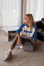 Pull doux à capuche bleu porté par une femme, assise, assise au sol, inscription AMOUR