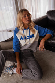 Pull doux à capuche bleu porté par une femme, assise, assise au sol, inscription