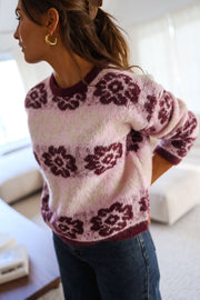 Pull à fleurs col rond porté par une femme, vue de trois-quarts, cheveux blonds, rideaux