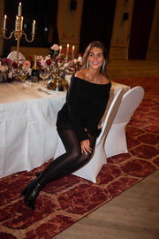 Pull loose à col bardot noir porté par une femme, silhouette entière, collants noirs, bottines