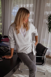 Pull cache-cœur à nouer gris porté par une femme, assise, fauteuil, nœud