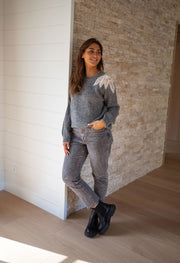 Pull à perles col rond gris porté par une femme, silhouette entière, mur en pierre, jean gris