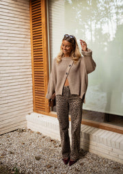 Pull boutonné col rond taupe porté par une femme, silhouette entière, mur en briques, pantalon gris