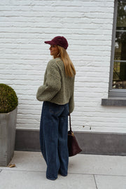 Pull doux à manches ballon porté par une femme, vue de dos, casquette bordeaux, buisson
