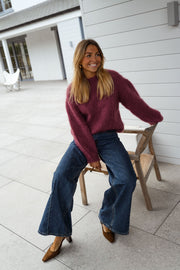 Pull ample aubergine col rond porté par une femme, assise, chaise en bois, jambes croisées