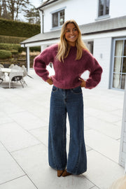 Pull ample aubergine col rond porté par une femme, vue de face, terrasse, mains sur les hanches