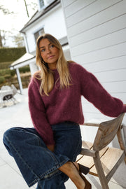 Pull ample aubergine col rond porté par une femme, assise, chaise en bois, mains sur le dossier