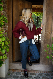 Pull ample doux col rond bordeaux porté par une femme, vue de face, plantes, sac à main