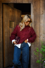 Pull ample doux col rond bordeaux porté par une femme, vue de trois-quarts, porte ouverte, jean bleu