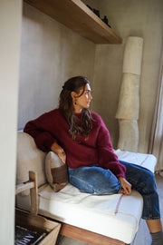 Pull ample doux col rond bordeaux porté par une femme, assise, banc blanc, coussin