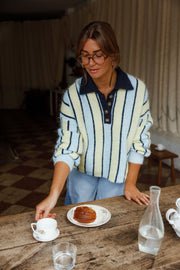 Pull ample à col boutonné bleu clair et crème à rayures porté par une femme, vue de face, à une table