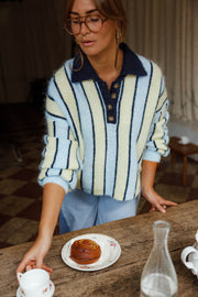 Pull ample à col boutonné bleu clair et crème à rayures porté par une femme, vue rapprochée, à une table