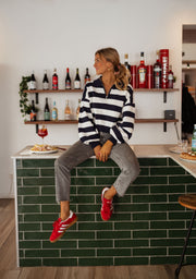 Pull rayé à col zippé porté par une femme, assise, assise sur le comptoir, baskets rouges