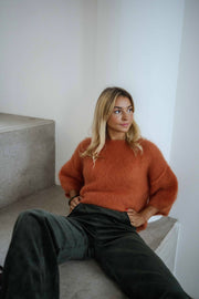 Pull col rond manches trois-quarts orange porté par une femme, assise, marches grises, jean noir