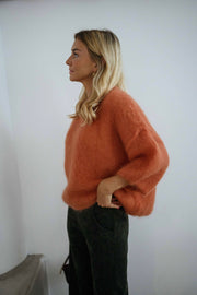 Pull col rond manches trois-quarts orange porté par une femme, vue de profil, mur blanc, manches bouffantes