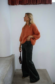 Pull col rond manches trois-quarts orange porté par une femme, vue de trois-quarts, escalier, sac noir