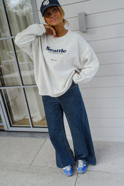 Pull ample à logo porté par une femme, vue de trois-quarts, casquette marine, baie vitrée