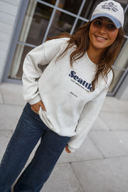 Pull ample à logo porté par une femme, vue de trois-quarts, casquette bleue, sourire