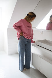 Pull loose à col rond porté par une femme, vue de dos, meuble blanc, jean large